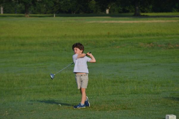 A young golfer takes his first swing at the “Fire in the Hole” golf 